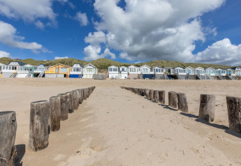 Cabañas de playa en la arena con postes de madera y dunas de césped en Dishoek, Zelanda, Países Bajos.