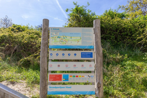 Panneau d’information à la plage de Dishoek aux Pays-Bas, avec carte, règles et directives, entouré de verdure.