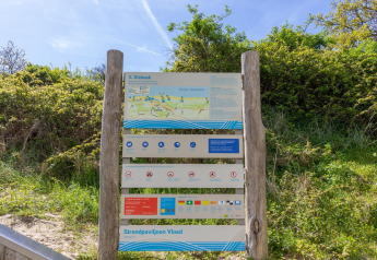 Cartello informativo sulla spiaggia di Dishoek nei Paesi Bassi con mappa, regole e linee guida tra il verde.