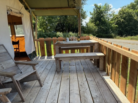 Holzterrasse mit Sitzbank und Tisch vor einem Safarizelt im Domaine Le Faulion, Frankreich, im Sommer.
