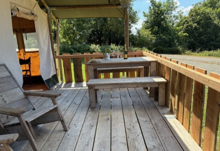 Wooden terrace with table and benches at a safari tent at Domaine Le Faulion, France, on a sunny day.