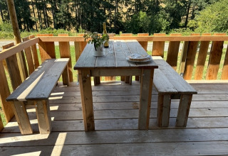 Holztisch und Bänke auf einer Terrasse im Freien mit Waldblick, aufgenommen beim Safari-Zelt Domaine Le Faulion.