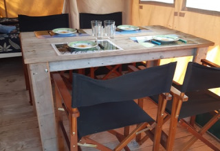 Tavolo e sedie in legno in una tenda safari al Domaine Le Faulion in Francia, apparecchiata per quattro.