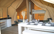 Interior of Safari tent 'WOOD' at Campsite des Tourbières in France showing dining table, beds, and kitchen.