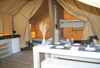 Interior of Safari tent 'WOOD' at Campsite des Tourbières in France showing dining table, beds, and kitchen.