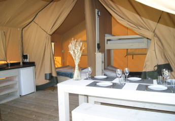 Interior of Safari tent 'WOOD' at Campsite des Tourbières in France showing dining table, beds, and kitchen.