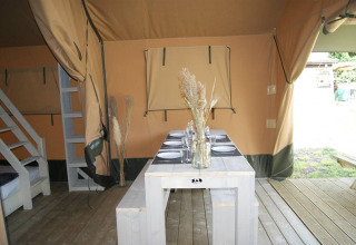 Interior de la tienda Safari «WOOD» en el Camping des Tourbières en Francia, con mesa y bancos de madera.