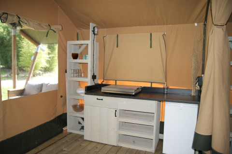 Kitchen area inside Safari tent 'WOOD' at Campsite des Tourbières in France with shelves and fridge.