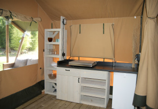 Køkkenområde i en safari-telt 'WOOD' på Camping des Tourbières i Frankrig med hylder og køleskab.