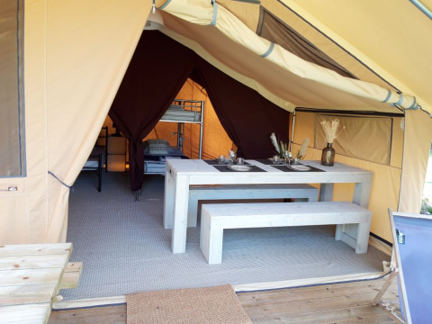 Interior of a safari tent at Campsite des Tourbières in France with a dining table and sleeping area.