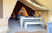 Interno di una tenda safari al Campeggio des Tourbières in Francia con tavolo da pranzo e letti.