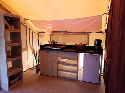 Indvendigt syn af et safari teltkøkken på Camping des Tourbières, Frankrig, med hylder og små køkkenapparater.