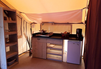 Interior view of a safari tent kitchen at Campsite des Tourbières in France with shelves, fridge and utensils.