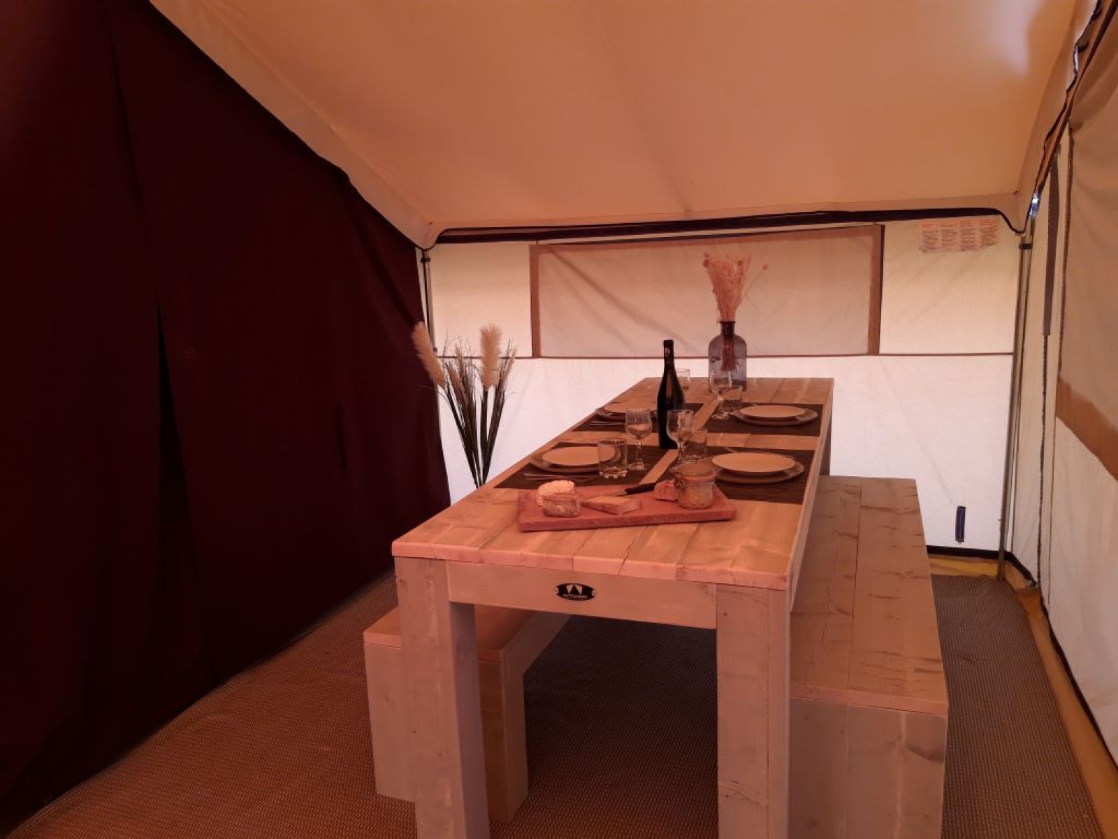 Het eetgedeelte in een safaritent op Camping des Tourbières in Frankrijk, met houten tafel en bank.