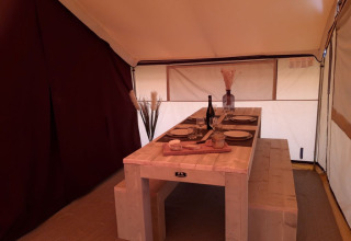 Interno di una tenda safari al Campeggio des Tourbières in Francia con tavolo e panca in legno apparecchiati.