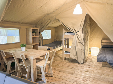 Intérieur de tente safari avec plancher en bois, meubles simples, lits superposés et table à manger.