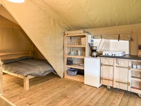 Intérieur d'une tente safari avec lit double et kitchenette au Camping des Randonneurs en France.
