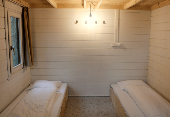 Twee eenpersoonsbedden in een gerenoveerde basic cabin met witte houten wanden bij Urban-Gardens Gent.
