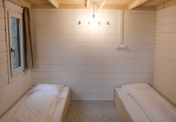 Twee eenpersoonsbedden in een gerenoveerde basic cabin met witte houten wanden bij Urban-Gardens Gent.