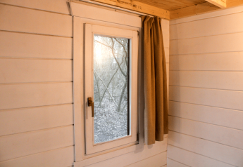 Interior view of a tiny house with white wooden walls, a window, and beige curtain in Gent, Belgium.