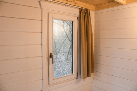 Binnenaanzicht van een tiny house in Gent met witte houten muren, raam en beige gordijn.