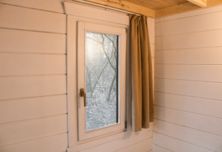 Binnenaanzicht van een tiny house in Gent met witte houten muren, raam en beige gordijn.