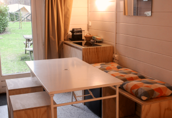 Gerenoveerde basic cabin in Gent, België, met eettafel, keukenhoek en uitzicht op de groene tuin.