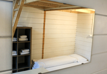 Interior of a renovated tiny cabin with bed, loft, and shelves with towels at Urban-Gardens Gent, Belgium.