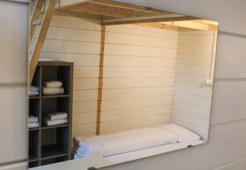 Intérieur d’une petite cabane rénovée avec lit, mezzanine et étagère à serviettes à Urban-Gardens Gent.