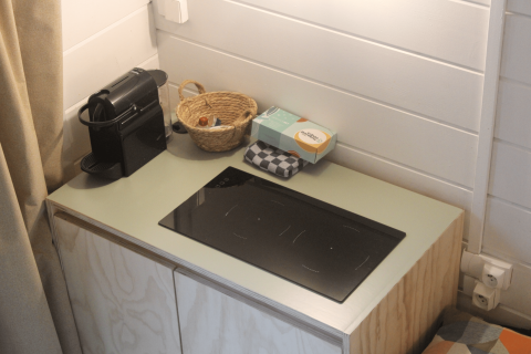 Kleine keukenhoek met koffiemachine, mandje, servetten en kookplaat in opgeknapte cabin in Gent.