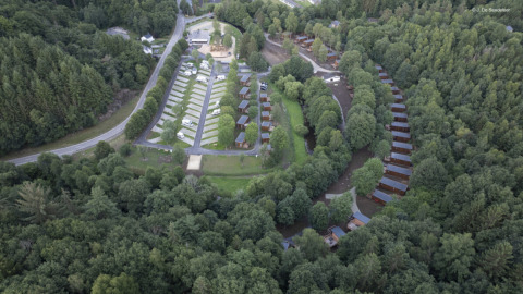 Luchtfoto van vakantiepark Le Hameau de l'Ourthe in België, met huisjes, campers en veel bomen.