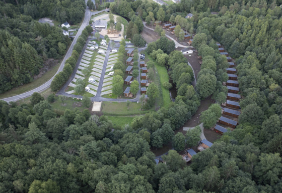 Luchtfoto van vakantiepark Le Hameau de l'Ourthe in België, met huisjes, campers en veel bomen.