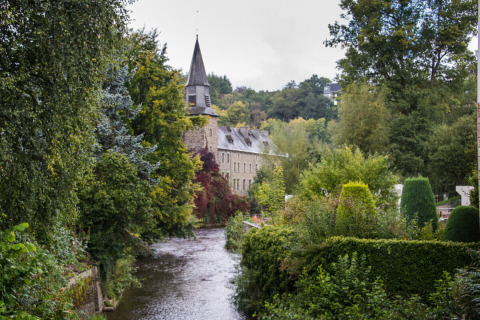 Scenic view of a stone building with a tower by a river at Le Hameau de l'Ourthe, lush Belgium countryside.