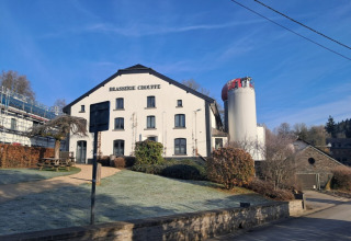 Edificio Brasserie Chouffe presso il parco vacanze Le Hameau de l'Ourthe, circondato da natura e cielo blu in Belgio.