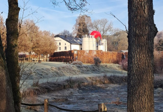 Vista su Le Hameau de l'Ourthe, parco vacanze in Lussemburgo belga, con alberi, recinzione e cupola rossa.