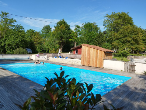 Piscina all'aperto al Campeggio des Tourbières, circondata da alberi e pedana in legno in Francia.