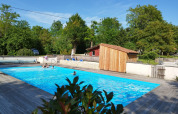 Outdoor swimming pool at Campsite des Tourbières, with trees and a wooden deck in Nouvelle-Aquitaine, France.