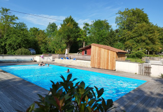 Buitenzwembad van Camping des Tourbières, met houten terras en veel groen in Nouvelle-Aquitaine, Frankrijk.