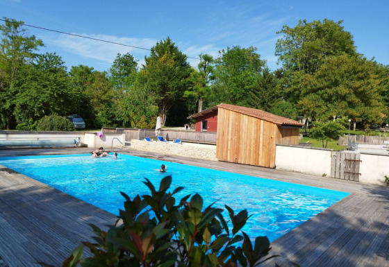 Piscina all'aperto al Campeggio des Tourbières, circondata da alberi e pedana in legno in Francia.