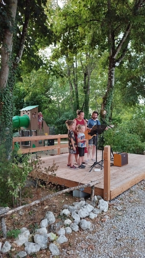 Famiglia e chitarrista cantano su un palco in legno al Campsite des Tourbières, vacanze in Nouvelle-Aquitaine.