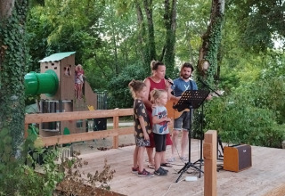 Famiglia e chitarrista cantano su un palco in legno al Campsite des Tourbières, vacanze in Nouvelle-Aquitaine.