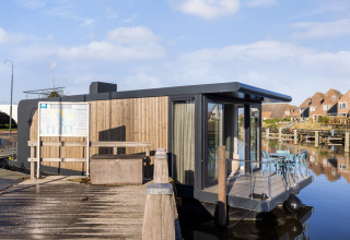 Moderne woonboot aan de Marina Lemmer in Nederland, aangemeerd met terras en huizen op de achtergrond.