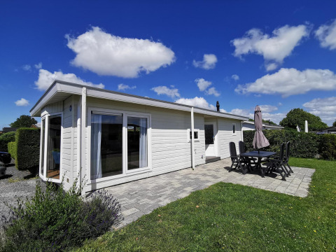 Foto de Chalet Basic, una cabaña blanca con terraza, sillas, mesa y cielo azul con nubes al fondo.