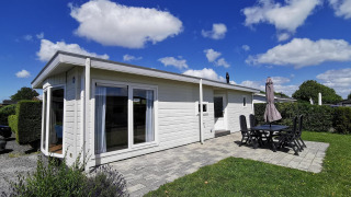 Foto de Chalet Basic, una cabaña blanca con terraza, sillas, mesa y cielo azul con nubes al fondo.