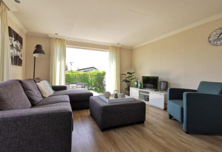 Salón en Chalet Basic en De Woudhoeve, Países Bajos, con sofá cómodo, decoración moderna y gran ventanal.