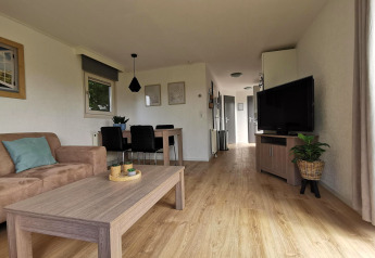 Lyst og moderne opholdsområde i Chalet Basic på De Woudhoeve i Holland med træmøbler og stor TV.