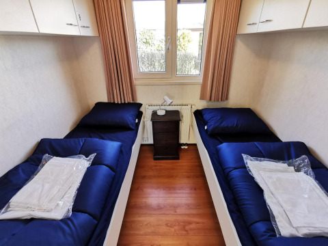 Dormitorio con dos camas individuales, ropa de cama azul oscuro y ventana en Chalet Basic, De Woudhoeve, Países Bajos.