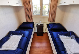 Dormitorio con dos camas individuales, ropa de cama azul oscuro y ventana en Chalet Basic, De Woudhoeve, Países Bajos.