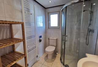 Baño moderno en Chalet Basic de De Woudhoeve, Países Bajos, con ducha curvada y estantería de madera.