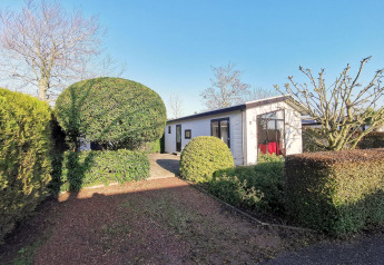 Moderne chalet kaldet Chalet Basic ved De Woudhoeve i Holland, omgivet af velplejede haver og buske.